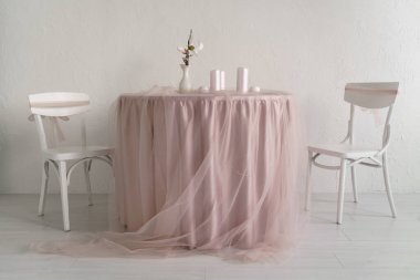 İki beyaz sandalye ve pembe elbiseli bir masa.