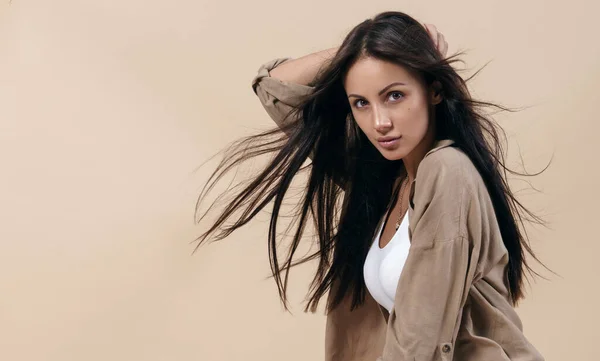 Portret van brunette meisje met vliegend gezond lang haar op beige achtergrond met kopieerruimte — Stockfoto