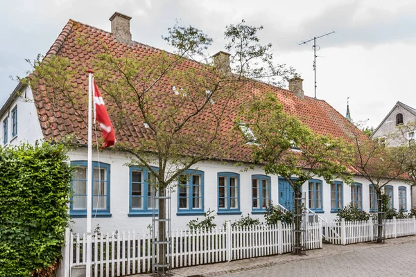 La bandera danesa fuera de una casa con ventanas azules y una cerca blanca —  Fotos de Stock