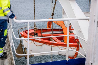 Denizci, Stena Naut feribotunun güvertesinde bir cankurtaran sandalının üstünde duruyor.