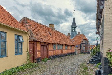 Old cobblestone-street with a red half-timbered house and the town hall in the background, Ebeltoft, Denmark, September 9, 2019