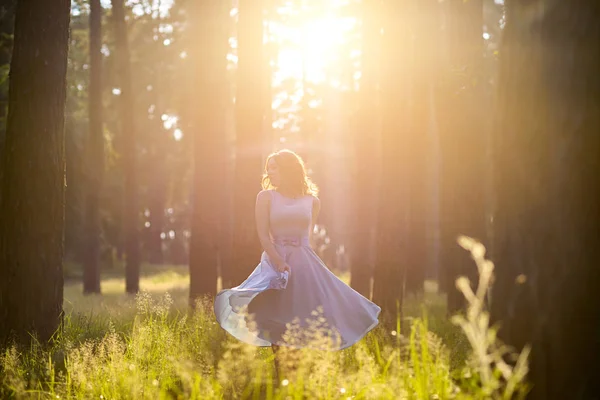 A girl in a light blue dress in the sun in the middle of the forest