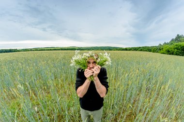 Papatya alan bir buket bir adamla bir buğday tarlanın ortasında duruyor