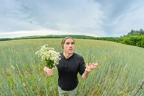 A man with a bouquet of daisies field stands in the middle of a wheat field