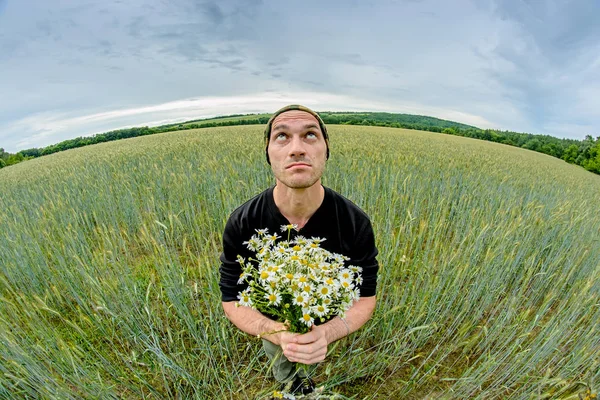 A man with a bouquet of daisies field stands in the middle of a wheat field