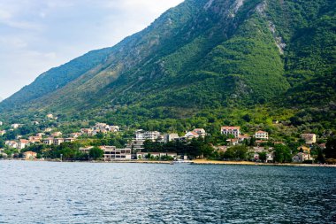 Deniz ve dağlar. Deniz kenarında evler vardır.