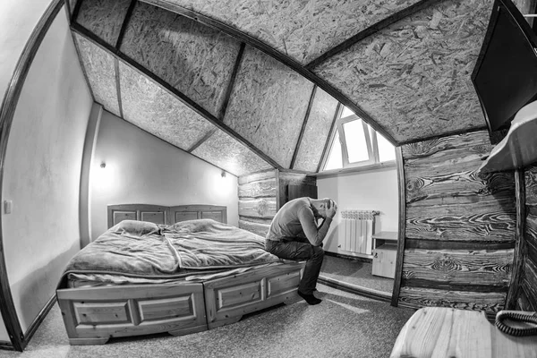 a man in a dress sitting on the edge of the bed holding his hands behind his head. Toning.black and white photo