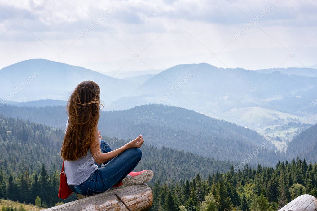 Girl with long hair sitting on a mountainside