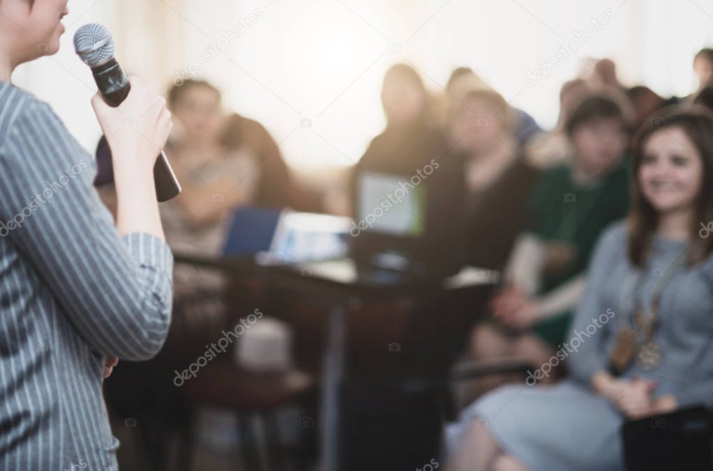 The speaker speaks with a microphone in front of a group of people. Photo is blurry