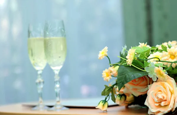 Желтые розы на фоне двух бокалов шампанского. Только розы в фокусе — стоковое фото