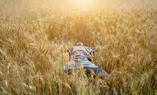 Ein Mann liegt in einem Weizenfeld und breitet seine Arme zur Seite aus — Stockfoto