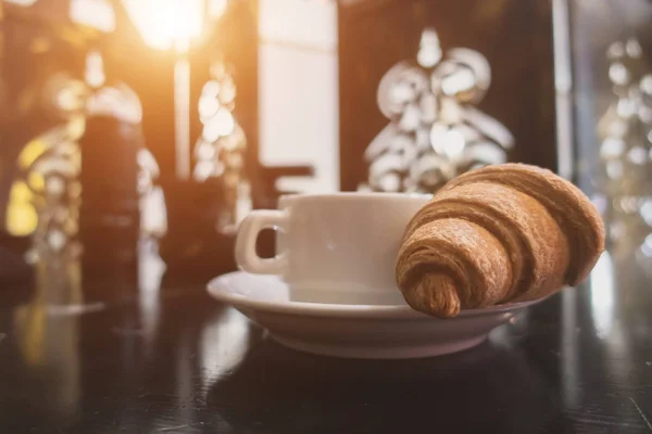 Croissant et tasse avec café sur la table. Près du fond se trouve la caméra — Photo