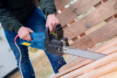 Tahta paleti elektrikli testereyle kesen bir adam. Paletlerden mobilya yapmak.