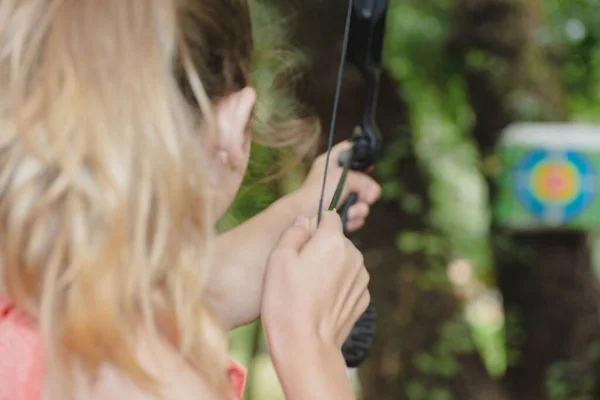 A girl shoots a bow at a target. The target is attached to the tree