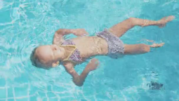 Lilla söta tjejen simmar på rygg i poolen i slow motion — Stockvideo