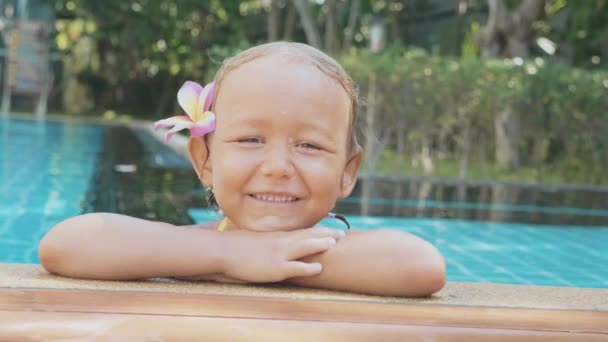 Портрет счастливой девочки, улыбающейся на краю бассейна в замедленной съемке — стоковое видео