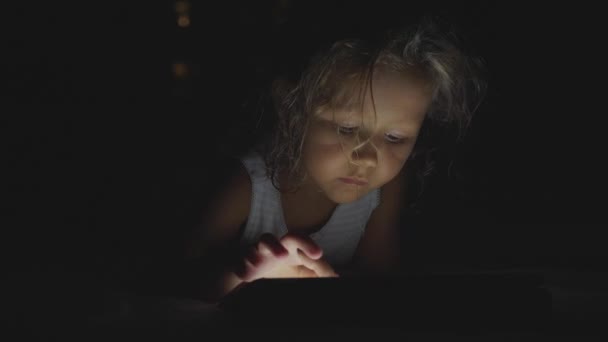 Pequena menina bonito deitado em uma cama e usando dispositivo tablet digital na hora de dormir . — Vídeo de Stock