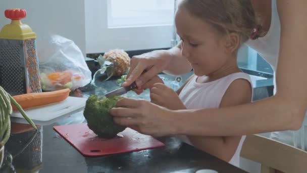 Jovem mãe ensinando cozinhar sua filha na cozinha doméstica . — Vídeo de Stock