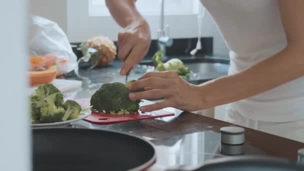 Молода жінка, що ріже броколі на домашній кухні . — стокове відео