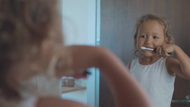 Pequeña niña linda cepillarse los dientes con un cepillo de dientes en el baño — Vídeo de stock