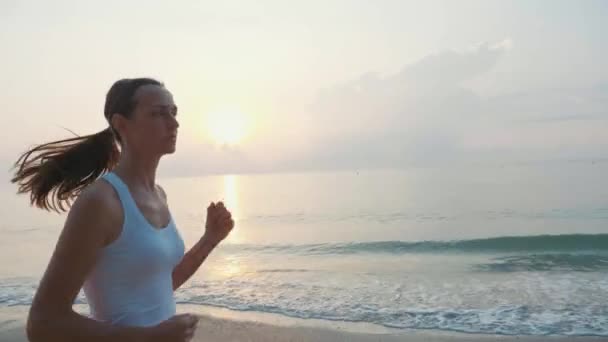 Steadicam atış genç çekici kadın güneş doğarken sahilde koşu — Stok video