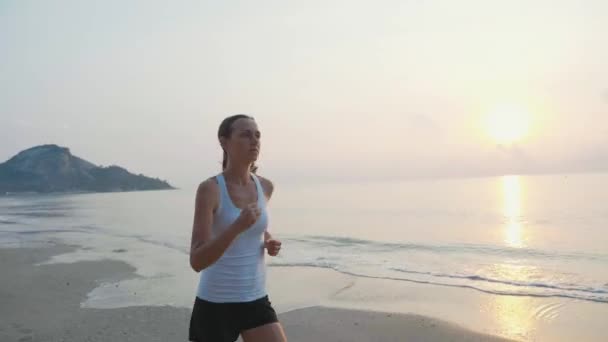 Steadicam-Aufnahme einer jungen attraktiven Frau, die bei Sonnenaufgang am Strand joggt — Stockvideo