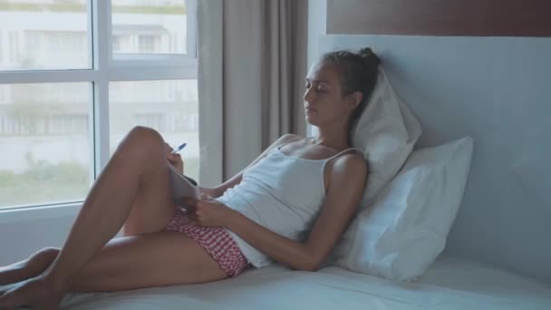 Mujer joven acostada en la cama y escribiendo páginas matutinas en el diario — Vídeos de Stock