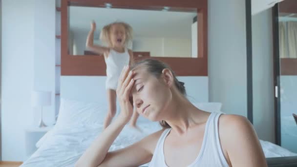 Upset mother with hyperactive child jumping on bed on the background — Stock Video