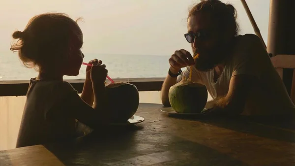 Father and daughter sits at seaview cafe and drinks coconuts together — Stock Photo, Image