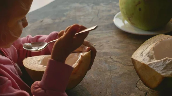 Niña linda comiendo coco por cuchara en la cafetería —  Fotos de Stock