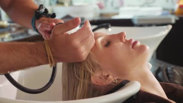 Männliche Stylistin wäscht blonden Frauenkopf in einem modernen Schönheitssalon — Stockvideo