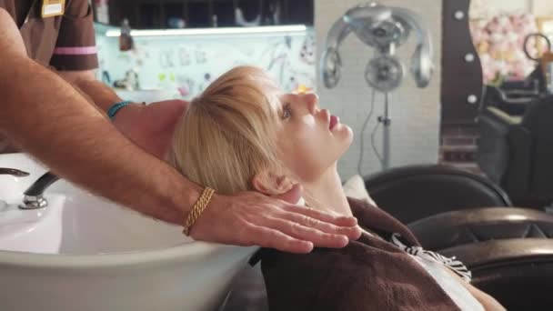 Mężczyzn stylista mycia blond womans głowę w nowoczesny salon kosmetyczny — Wideo stockowe