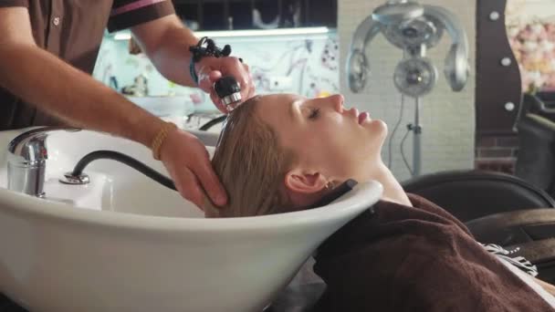 Αρσενικό στυλίστας πλύσιμο μια ξανθιά γυναικείο κεφάλι σε ένα μοντέρνο σαλόνι ομορφιάς — Αρχείο Βίντεο