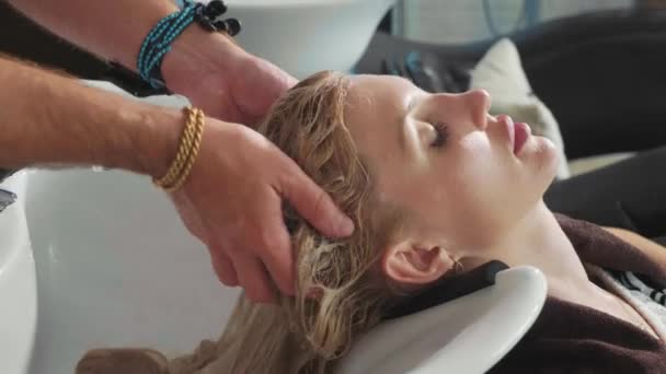 Homme styliste laver une tête de femme blonde dans un salon de beauté moderne — Video