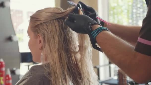 Парикмахер распутал волосы белокурой клиентки в салоне красоты — стоковое видео