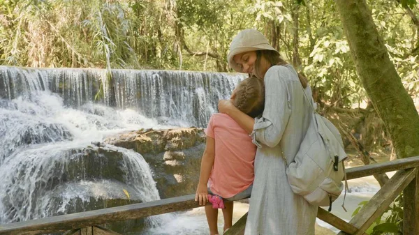 Uma jovem mãe e sua linda filha descansando contra a cascata de uma cachoeira — Fotografia de Stock