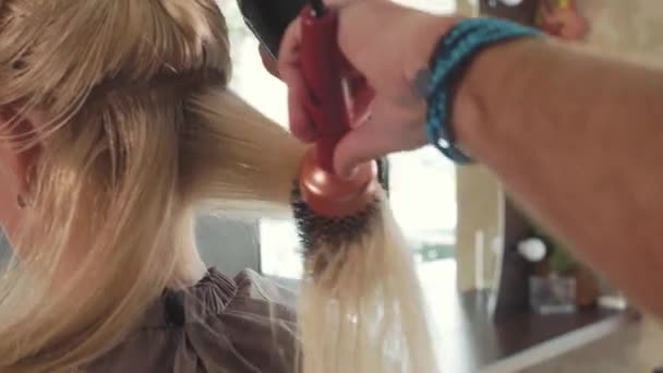 Αρσενικό κομμωτή που χτενίζει τα μαλλιά να ξανθιά κοπέλα στο σαλόνι ομορφιάς, γκρο πλαν — Αρχείο Βίντεο