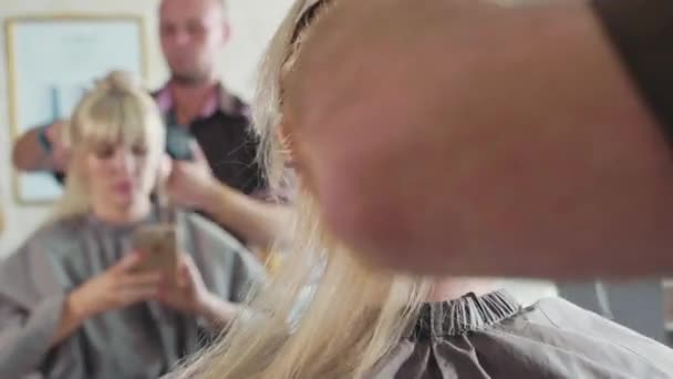 뷰티 살롱에서 금발 여자에 게 머리를 빗질 하는 남성 미용사 클로즈업 — 비디오