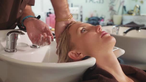 Männliche Stylistin wäscht blonden Frauenkopf in einem modernen Schönheitssalon — Stockvideo