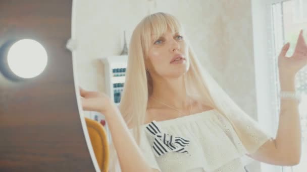 Молода жінка дивиться на себе в дзеркало і виправляє зачіску після перукарні — стокове відео