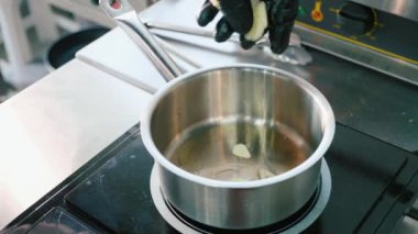 El eldiven Şef kıyılmış sarımsak soslu tavada koyar.