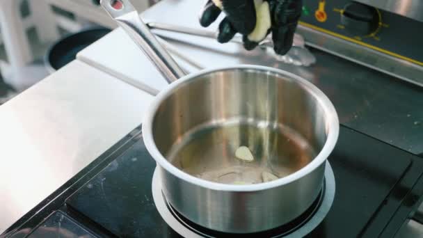 Рука шеф-повара в перчатках кладет нарезанный чеснок в сковороду для соуса — стоковое видео