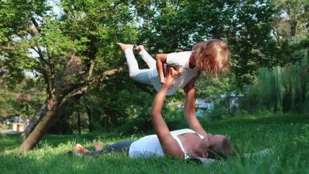 Joven madre deportista entrenando a su pequeña hija linda haciendo ejercicio de yoga — Vídeos de Stock