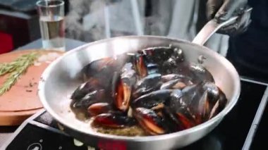 Tıslayan midye tava içinde. Şef deniz ürünleri petrol ve baharat ile karıştırma