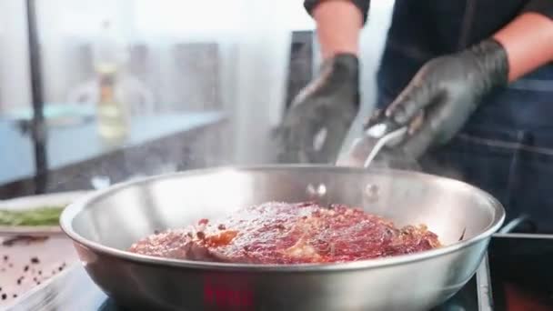 Kuchař používá kleště, aby se smažené šťavnaté maso steak v pánvi smažení, zblízka. — Stock video