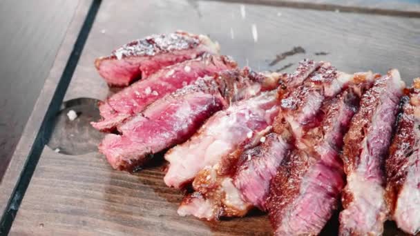 Nahaufnahme des Chefs streut ein großes Salz auf das gehackte gebratene Fleischsteak — Stockvideo