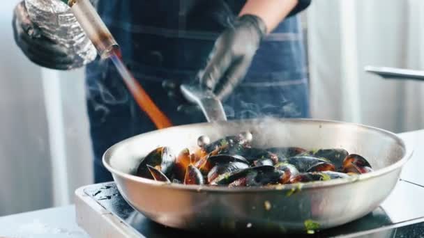 Chef con quemador de gas para preparar mejillones en sartén close-up cámara lenta — Vídeos de Stock