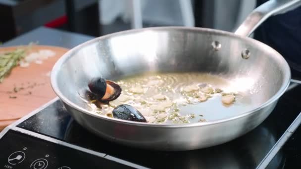 Chef pone mejillones en la sartén silbando con aceite y ajo . — Vídeos de Stock