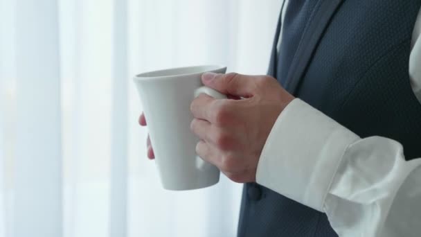 Руки с чашкой человека в костюме стоит у окна — стоковое видео