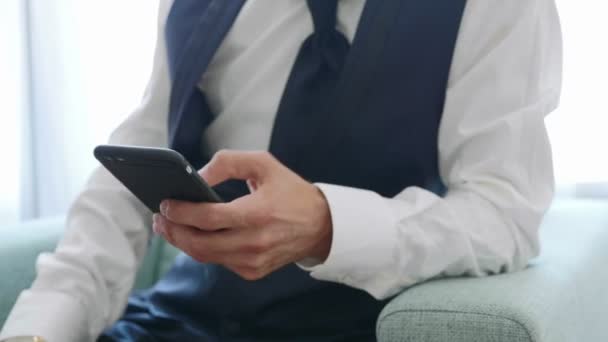 Manos con teléfono inteligente del hombre en traje se sienta en el sillón — Vídeo de stock